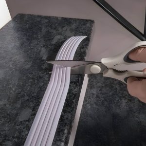Cutting white adhesive strip with scissors on surface.